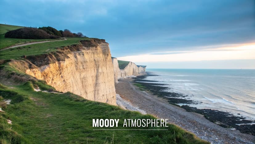 Dramatic white cliffs overlook a serene blue ocean under a cloudy sky with a grassy path.